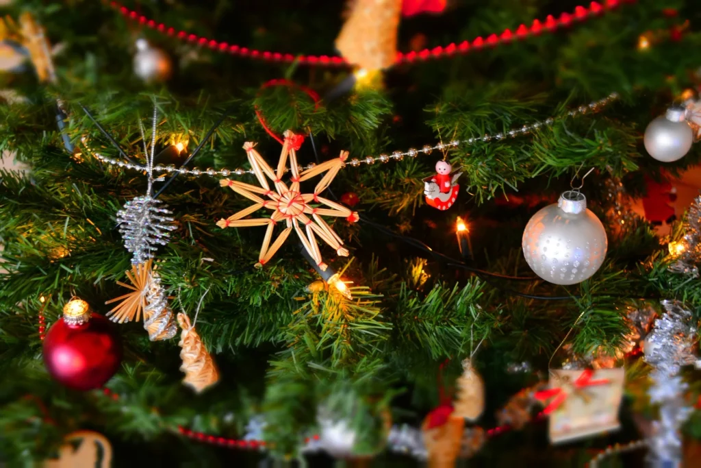 A festive Christmas tree decorated with red and silver ornaments, a straw star, and warm twinkling lights.