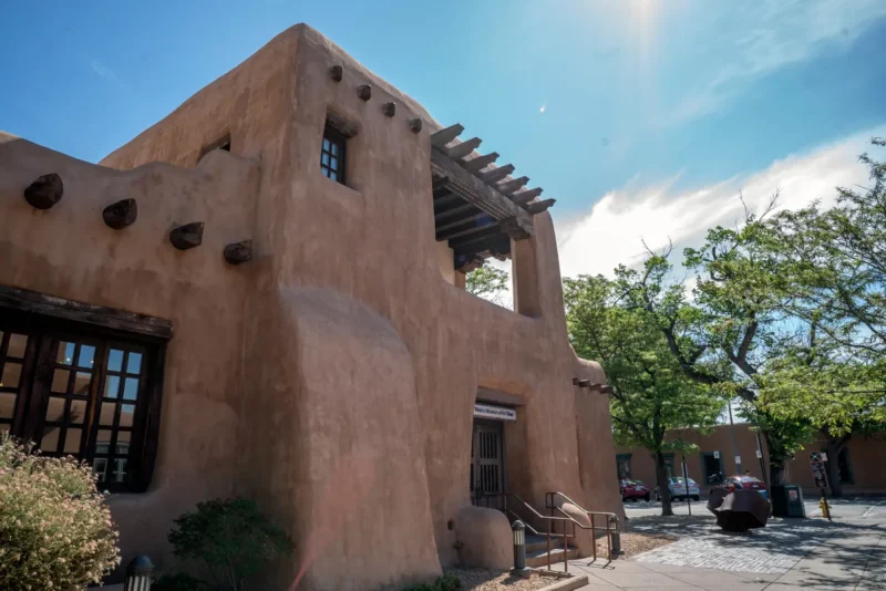 Close-up of a large, earthen-toned Pueblo Revival building featuring exposed wood vigas and a museum shop entrance.