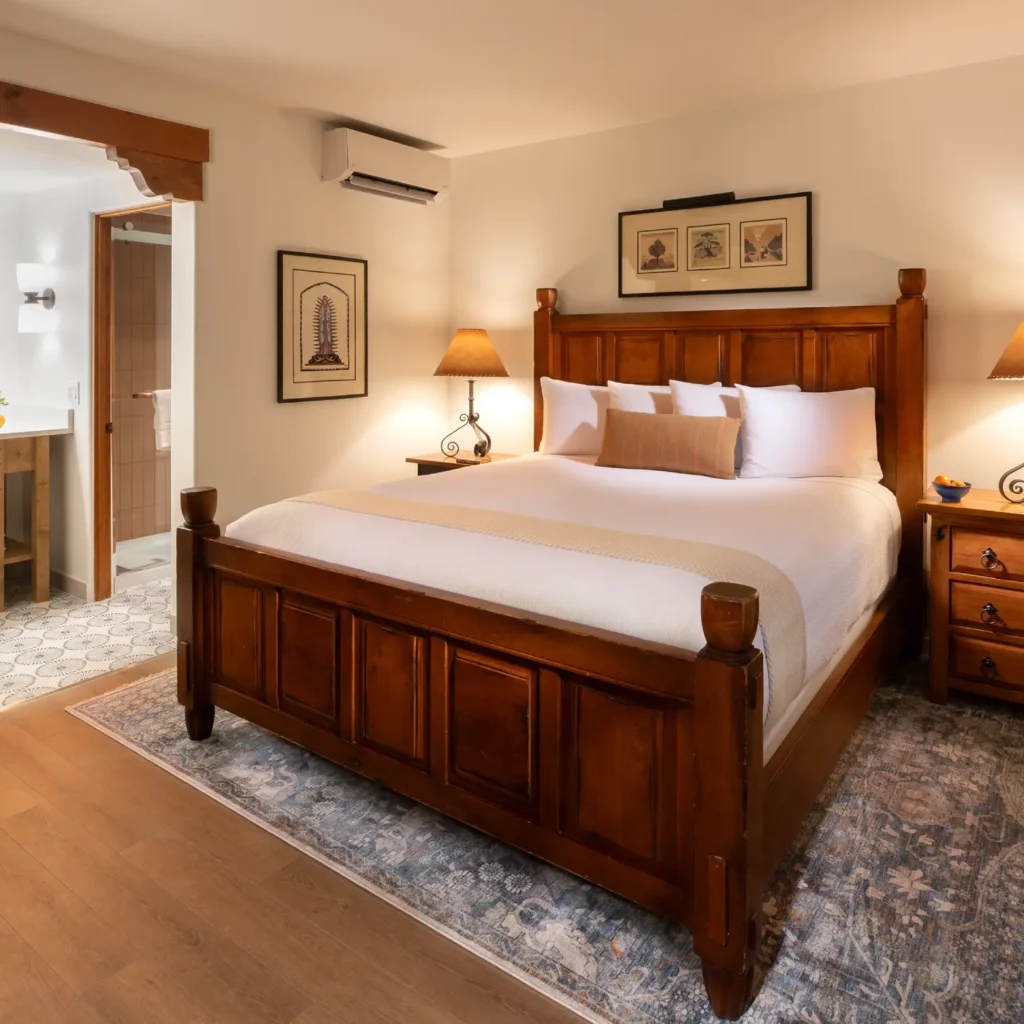 King bedroom suite featuring a large dark wood bed, cozy lighting, and an archway entrance to the private bathroom in a Napa Valley hotel.