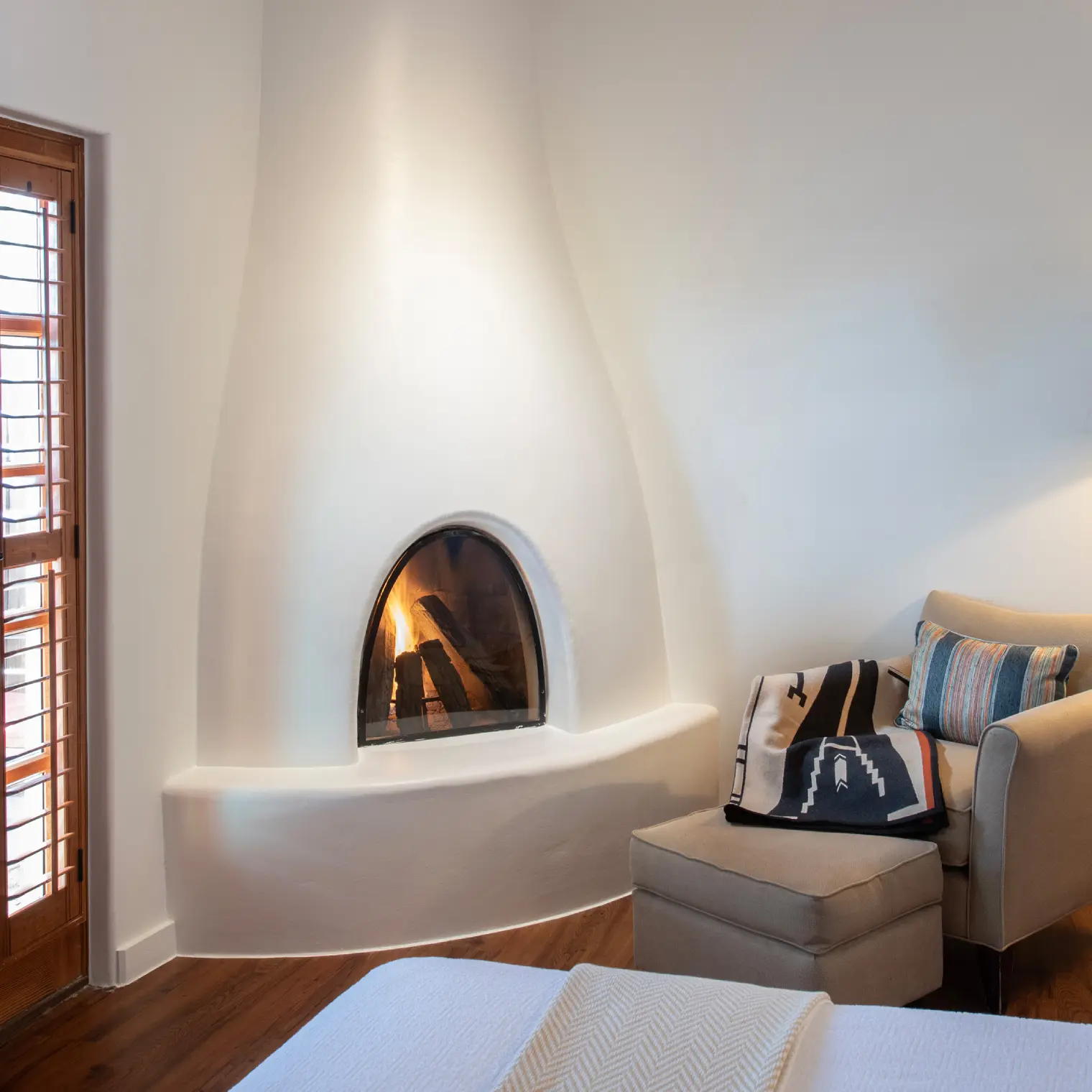 Cozy hotel room featuring a kiva fireplace, an armchair, and wooden shutters, appealing to hotels in Napa CA guests.