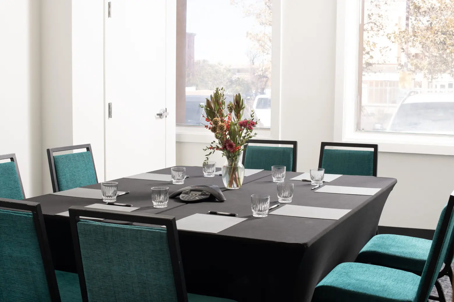 Modern meeting room setup with a conference table, teal chairs, and bright windows, ideal for a Napa Valley event venue.