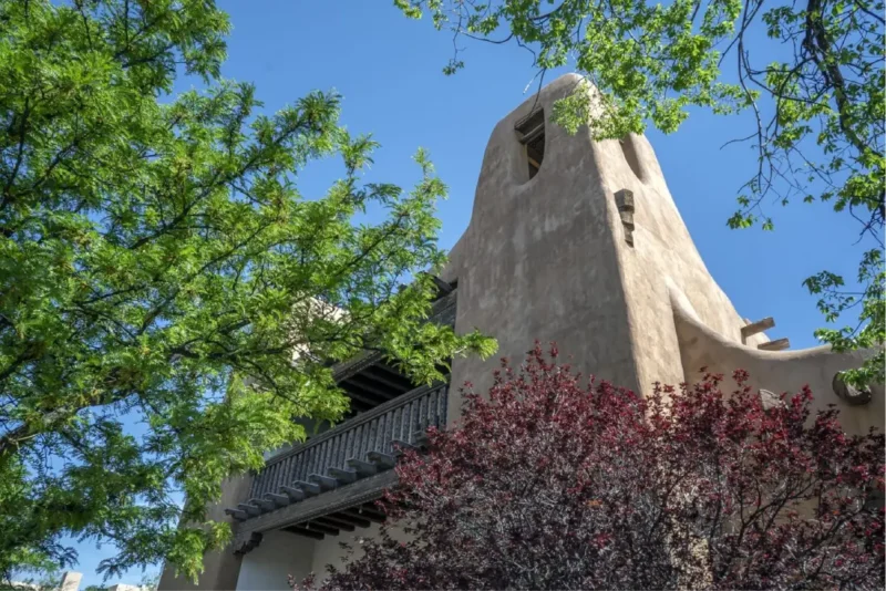 Piñon Court's curving adobe hotel building in Napa Valley featuring a dark wood balcony under the blue sky.