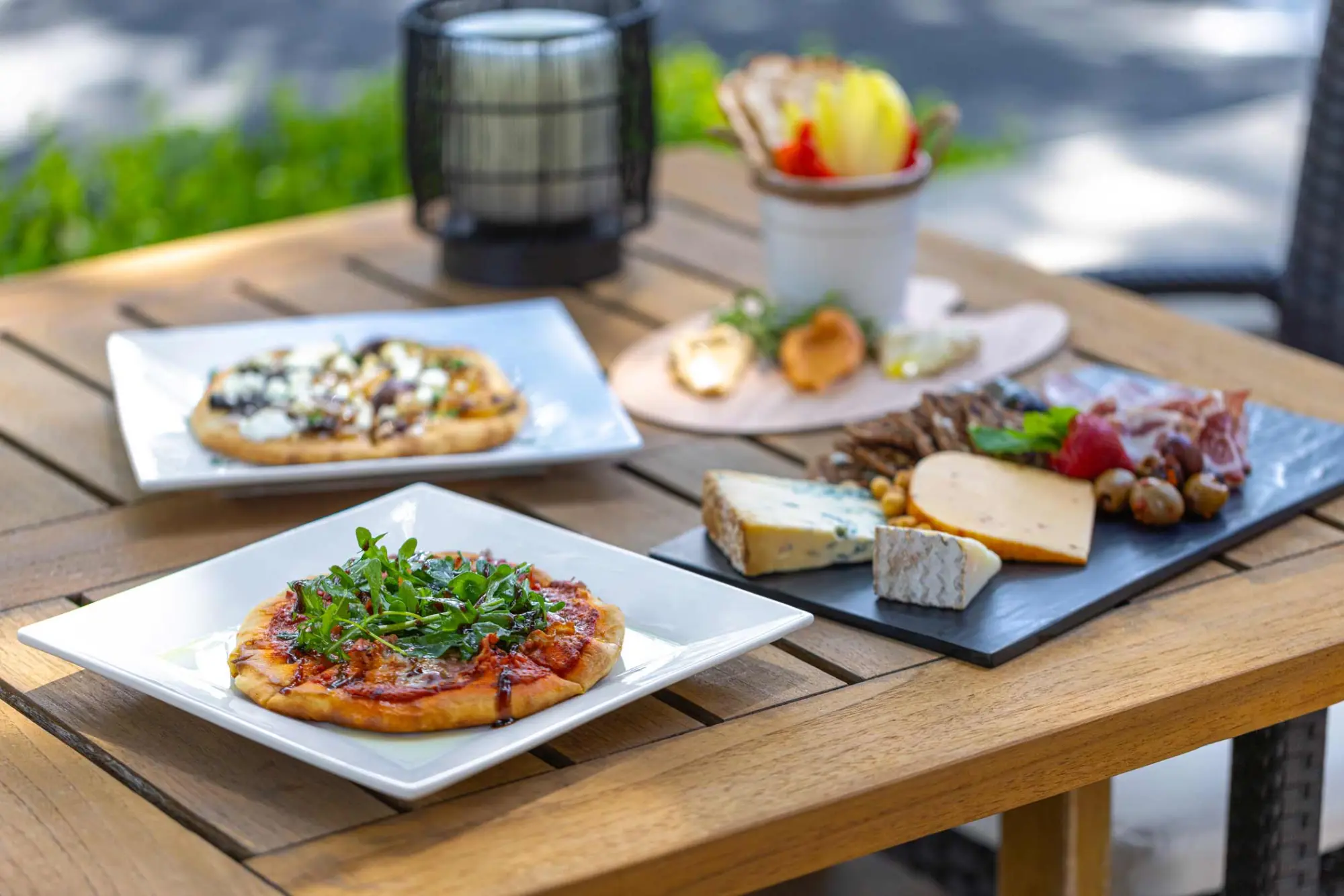 Gourmet flatbreads and a cheese and charcuterie board served outdoors on a wooden table at Napa CA hotels.