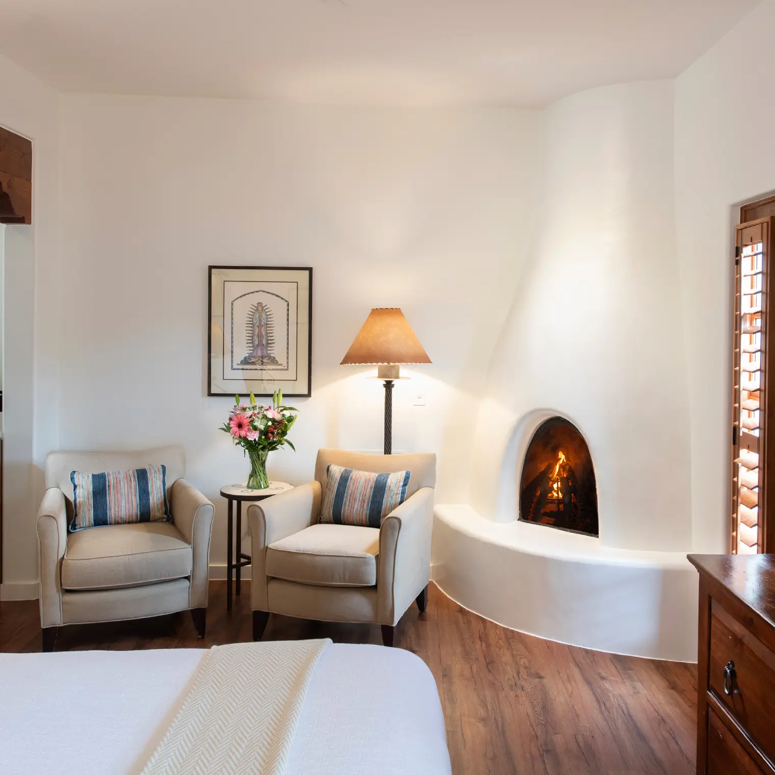 Cozy corner of a napa valley hotel suite featuring two armchairs and a lit adobe fireplace.