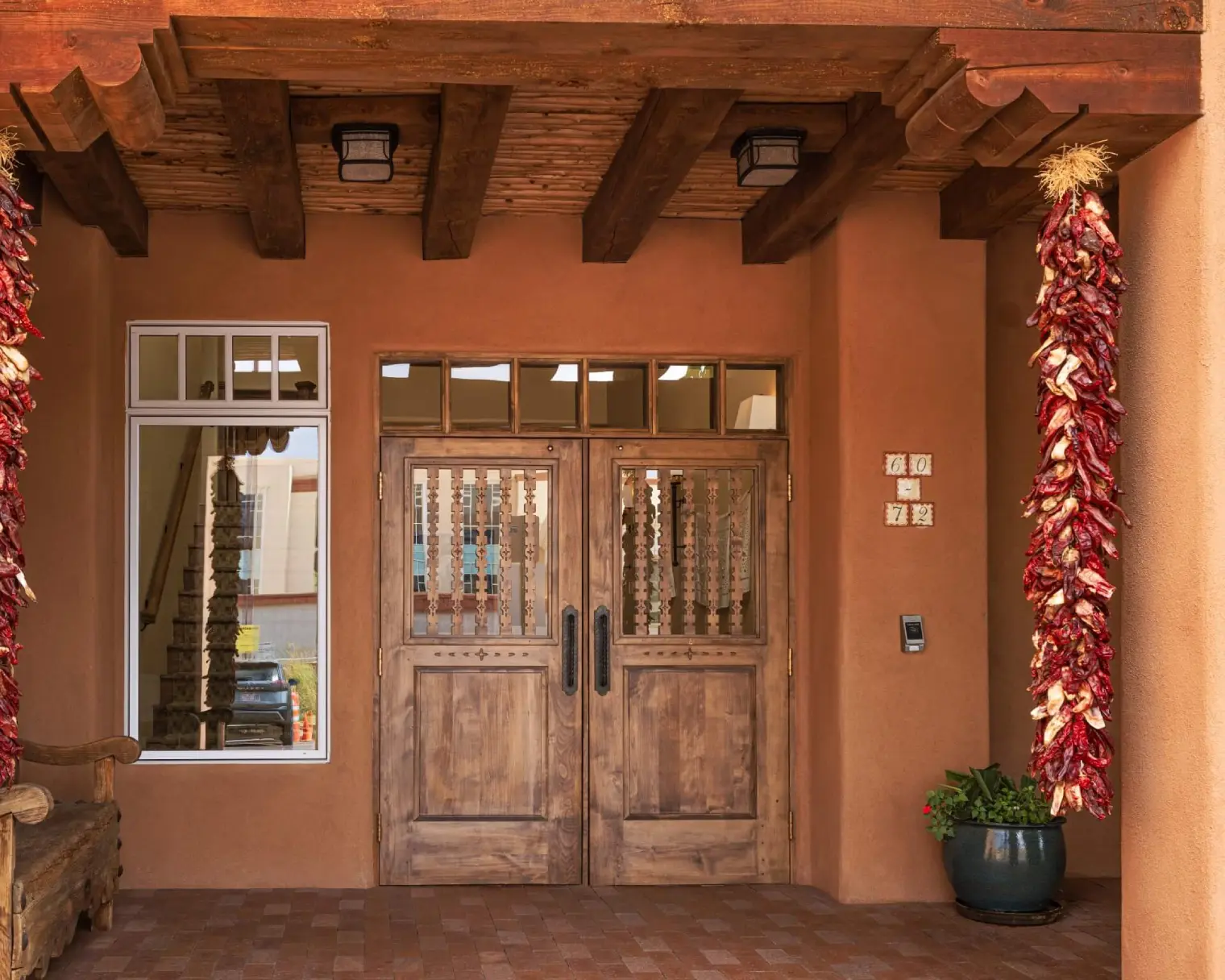 Santa Fe style hotel entrance featuring rustic wooden doors, adobe walls, and hanging chile ristras.