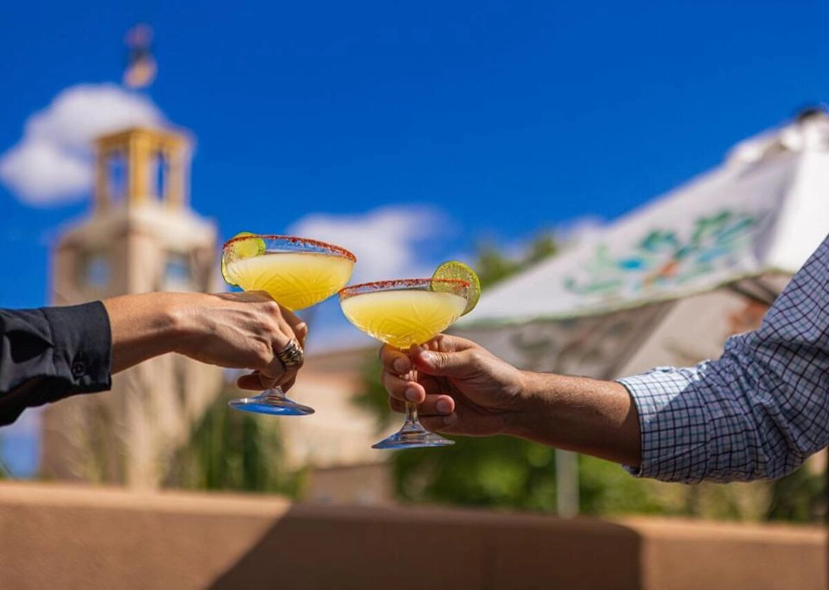 Two people toasting with salty margaritas outdoors, highlighting the leisure available at Santa Fe, NM hotels.