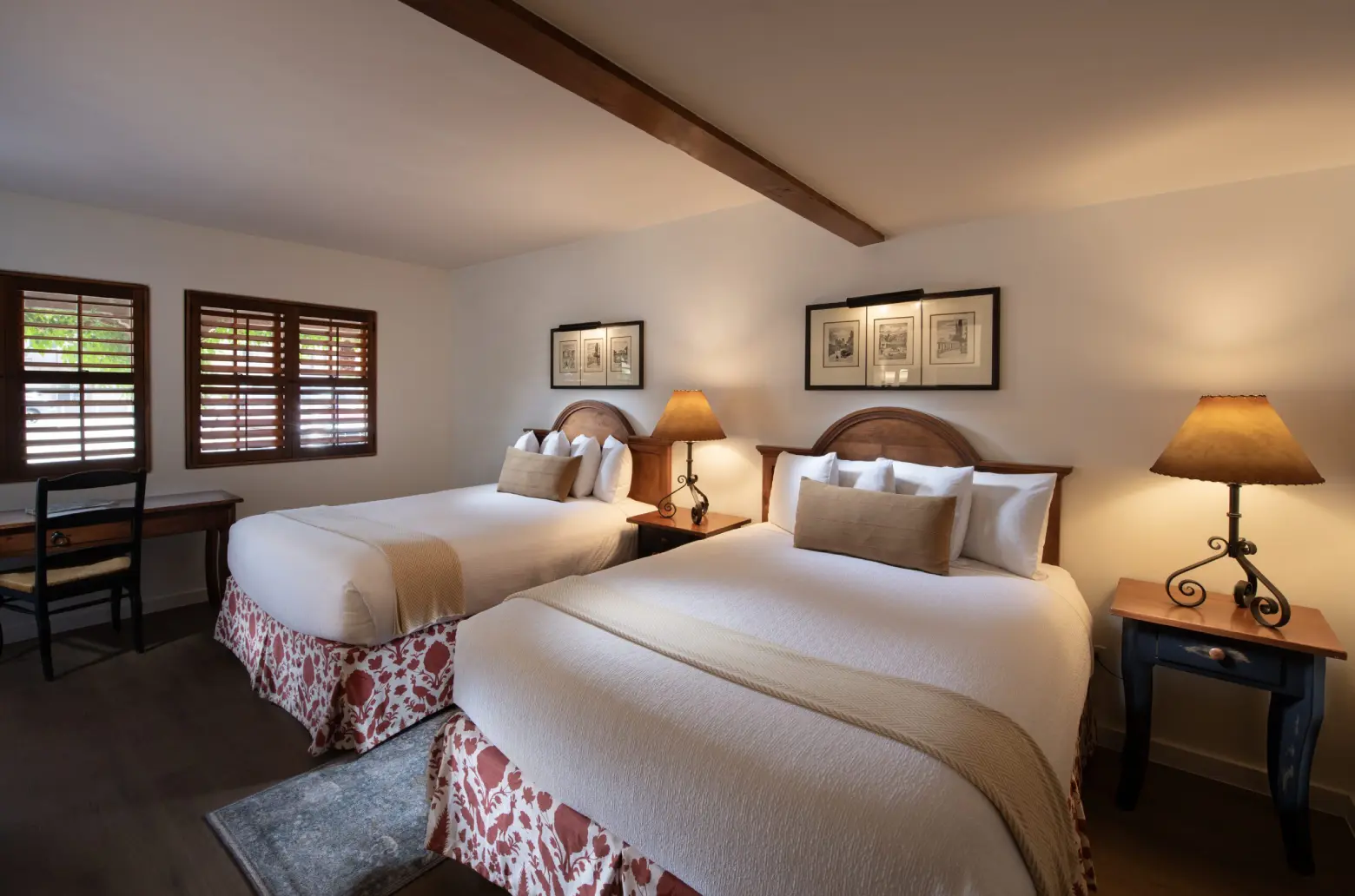 A hotel room with two beds, a desk, and lamps.