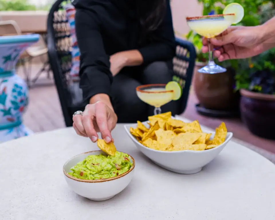 A table with a bowl of guacamole, a bowl of tortilla chips, and two margaritas.