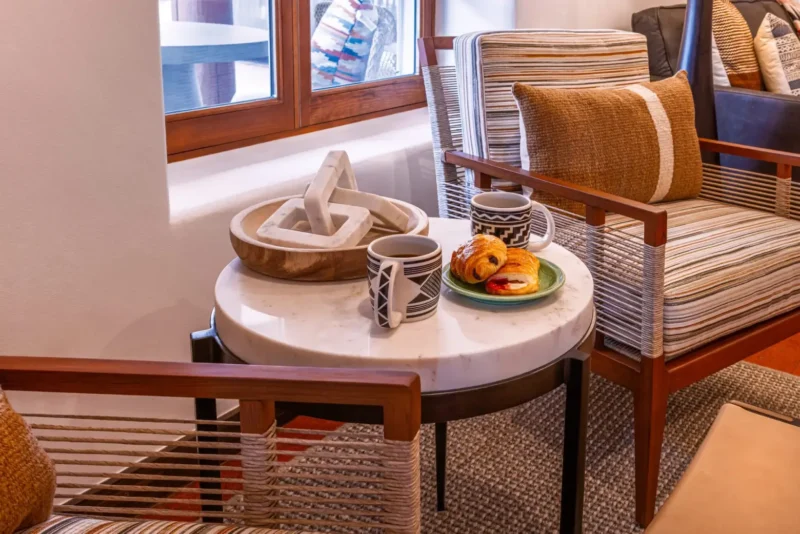 Two coffee mugs and croissants rest on a marble side table between striped chairs, perfect for breakfast in Napa CA.