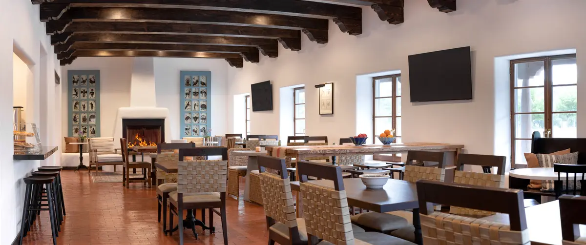 A large, well-lit lobby with a fireplace, wooden beams, and several tables and chairs.