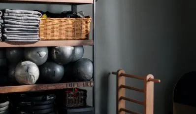 Modern shelving unit in a fitness room stocked with stability balls, stacked grey towels, and workout equipment.