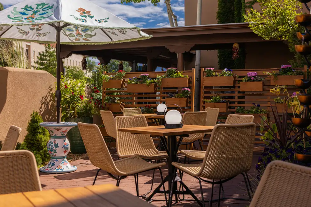 Sunny outdoor dining patio with wicker seating, wooden tables, and planters, perfect for breakfast in Santa Fe, NM.
