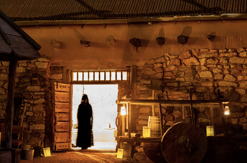 A stone-walled exterior with a wooden door and candlelight